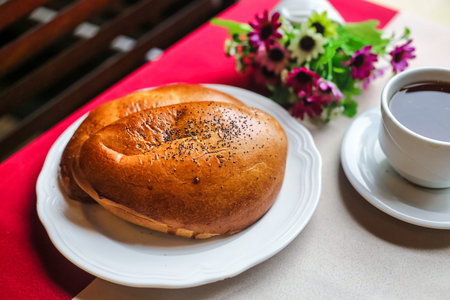 A white plate is seen with a bagel placed beside a cup of coffee.