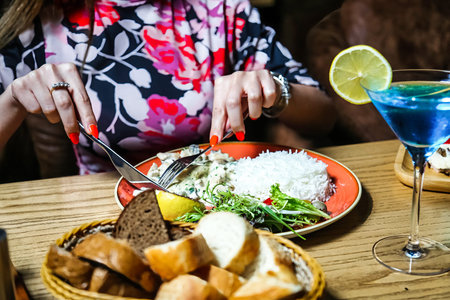 A woman sits at a table, enjoying a meal with a plate of delicious food in front of her.