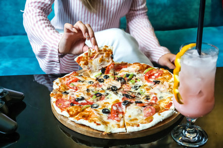 A woman sits at a table enjoying a pizza and a drink.
