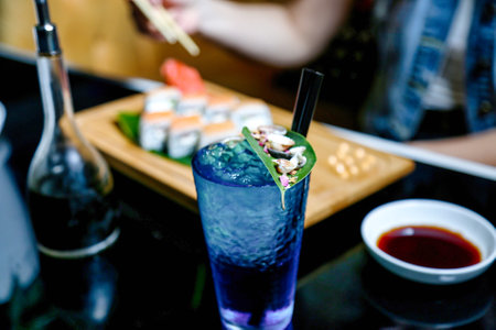 A glass of blue liquid positioned next to a plate of sushi, showcasing an enticing combination of flavors.の写真素材