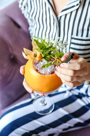 A woman is seated on a couch, holding a drink in her hand.の写真素材