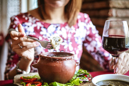 A woman is seated at a table, enjoying a plate of food and savoring a glass of wine.の写真素材