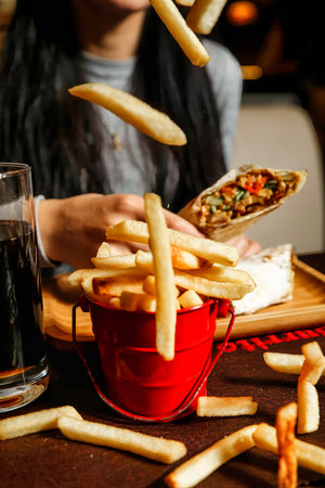 A person sitting at a table, enjoying a meal of fries and a refreshing drink.