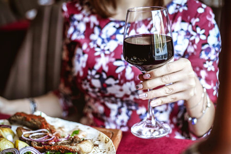 A woman is sitting at a table, with a plate of food and a glass of wine in front of her, enjoying...