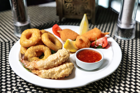 A white plate filled with a variety of fried food, such as chicken wings, onion rings, and French fries, served with a dipping sauce on the side.の写真素材