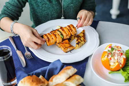 A woman carefully adds a skewer of food to a plate in a precise and deliberate manner.