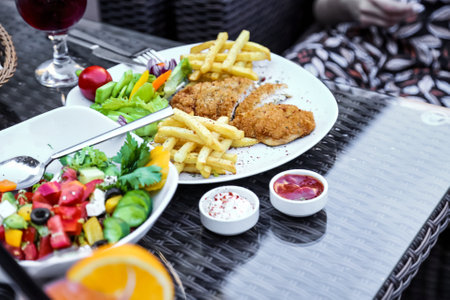 A tantalizing composition featuring a plate filled with succulent fried chicken, crispy French fries, refreshing salad, and a glass of red wine.の写真素材