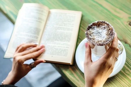 A person sits at an outdoor cafe, engrossed in a book, while holding a delicious pastry.の写真素材