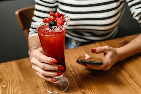 A woman sitting at a table, holding a drink in her hand.