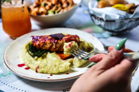 A person holds a silver fork over a colorful plate of delicious food, ready to take a bite.の写真素材