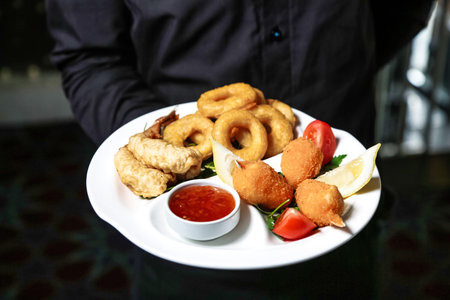 A person holds a plate filled with onion rings and ketchup, ready to enjoy the tasty meal.
