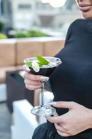A woman holds a martini glass containing a green leaf, showcasing an elegant cocktail garnish.の写真素材