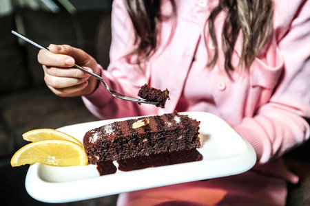A womans hand holds a white plate with a delicious piece of cake on it.