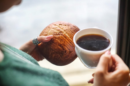 A woman is holding a cup of coffee and a piece of bread.