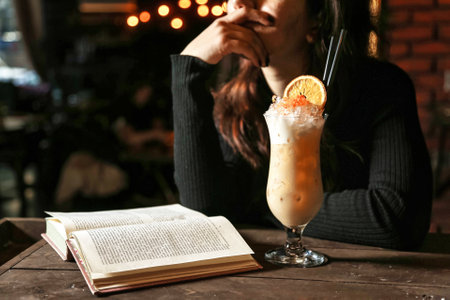 A woman sitting at a table, engrossed in a book while sipping on a drink.の写真素材