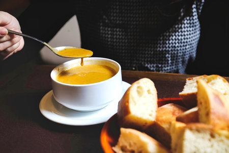 A bowl filled with hot and aromatic soup, garnished with a spoon placed beside it on a table.