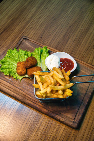 A close-up shot of fried chicken nuggets, french fries, and dipping sauces on a wooden board.