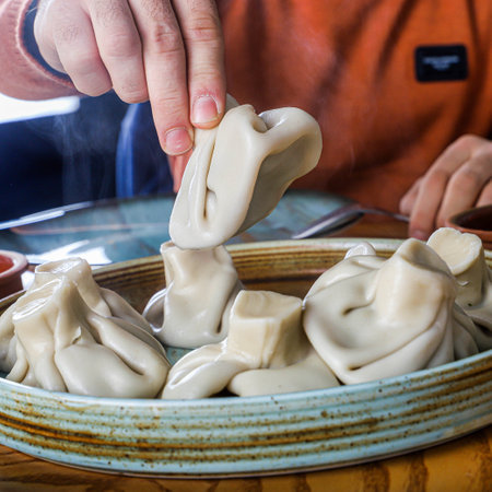 A hand picks up a steaming Khinkali dumpling from a plate of freshly prepared Georgian food.の写真素材