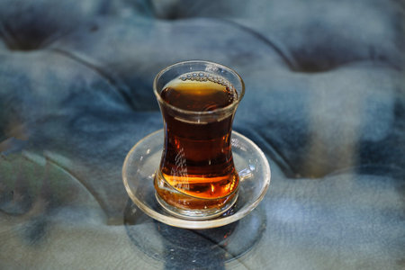 A glass of Turkish tea sits on a clear glass table with a blue tablecloth.