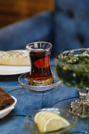 A glass of tea with lemon wedges on a blue tablecloth, with a piece of chocolate nearby.
