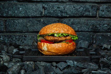 A fresh, juicy burger rests on a black grill, surrounded by charcoal.の写真素材