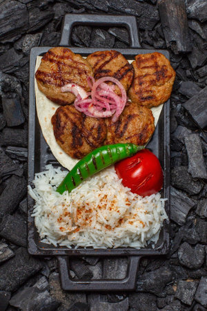 Grilled meatballs served with rice, green pepper, and red tomato.