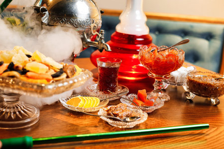 A table set with a traditional hookah, a teapot, steaming tea, and various sweet snacks.