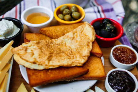 A close-up of fried egg on toast, surrounded by olives, jam, and other spreads.