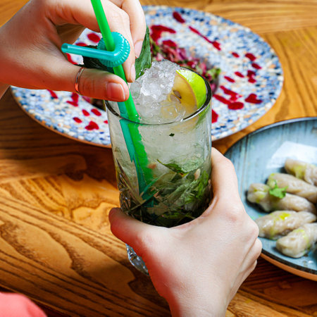A person holds a glass of a refreshing mint and lime drink with ice, garnished with fresh mint.の写真素材