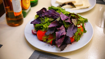 A plate of fresh greens, tomatoes, and onions on a white table.の写真素材