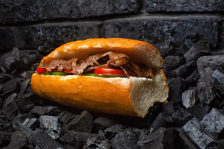A freshly prepared doner sandwich with meat, tomato, cucumber, and sauce, served on a bed of charcoal.の写真素材