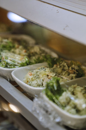 A close-up of prepared salads in clear plastic containers displayed in a white refrigerator case.の写真素材