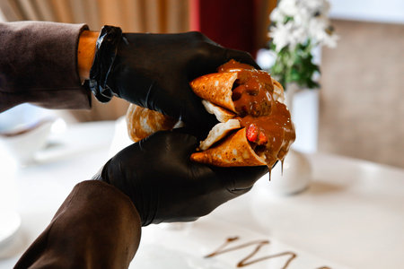 A hand wearing a black glove holds a chocolate-covered crepe with a white background in the background.の写真素材