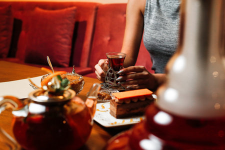 A woman sits at a table in a cafe, holding a glass of tea and enjoying dessert with a teapot and...