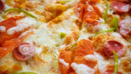 A close up of a slice of pizza with pepperoni, green peppers, and melted cheese.の写真素材