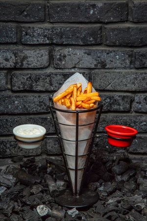 French fries in a metal cone with dipping sauces on a bed of charcoal.の写真素材