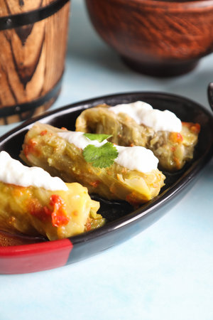 Closeup of three stuffed cabbage rolls on a black and red plate topped with yogurt sauce and...