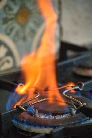 A vibrant orange flame rises from a gas burner in a well-lit kitchen, showing the efficient cooking method. The background features decorative tiles.の写真素材