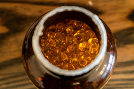 Close view of shiny, amber capsules inside a jar resting on a rustic wooden surface, showing their...