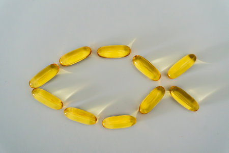 Yellow gelatin capsules are creatively arranged to form the shape of a fish, set against a bright white surface, highlighting their smooth texture and shine.の写真素材