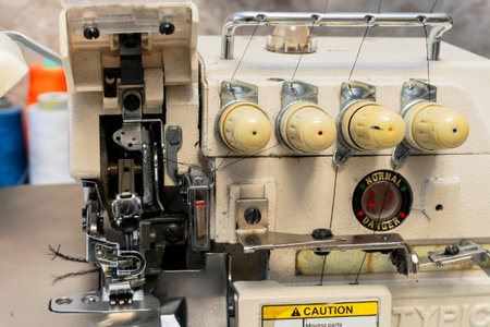 This close-up view reveals a vintage sewing machine with various spools of thread in the background,...