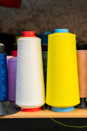 Brightly colored spools of thread are neatly arranged on a shelf in a sewing studio, showing various...