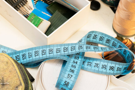A measuring tape is coiled around various craft supplies on a workspace. Scissors, pins, and spools of thread are also visible, indicating preparation for a project.の写真素材