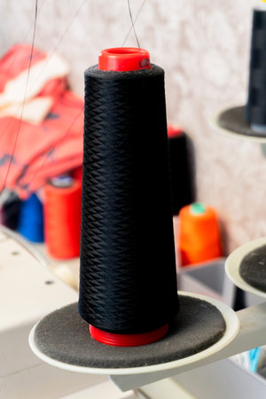 A large spool of black thread rests on a sewing machine in a textile workshop. Bright colored spools...