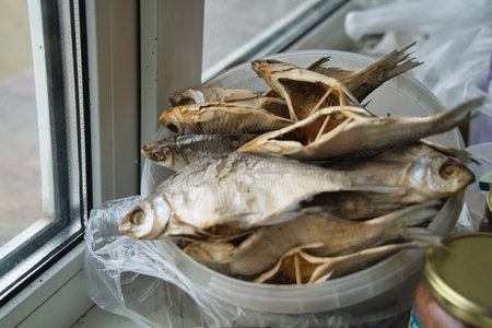 A bowl filled with dried fish sits on a windowsill, showing the catch in a domestic kitchen setting. Natural light illuminates the scene, enhancing the textures.の写真素材