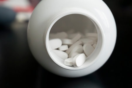 White oval tablets are scattered around a ceramic container on a dark table surface, highlighting a potential health or wellness scenario.の写真素材