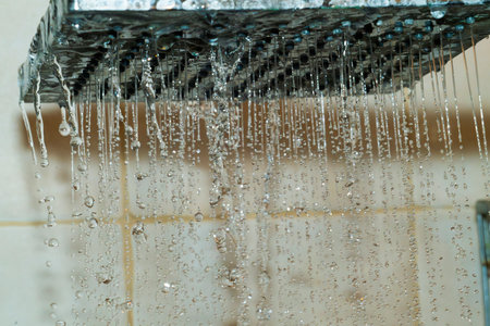 Water cascades down from a contemporary showerhead, creating droplets that glisten in the bright bathroom. The tiles reflect a clean and modern atmosphere.の写真素材