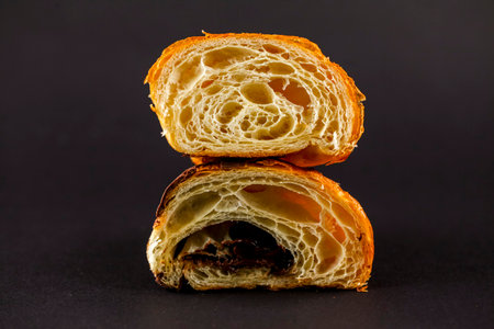 A freshly baked croissant is cut in half, revealing a soft, flaky interior with a generous chocolate filling. The dark background enhances its appeal.の写真素材