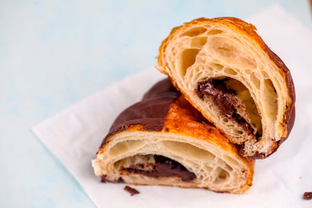 A delicious chocolate croissant cut in half reveals rich filling inside. It rests on a white napkin, showing its flaky layers and glossy top crust.の写真素材
