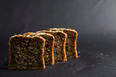 Freshly cut slices of multigrain bread are arranged neatly, highlighting their texture and color against a dark backdrop. Light casts soft shadows, enhancing the detail.の写真素材